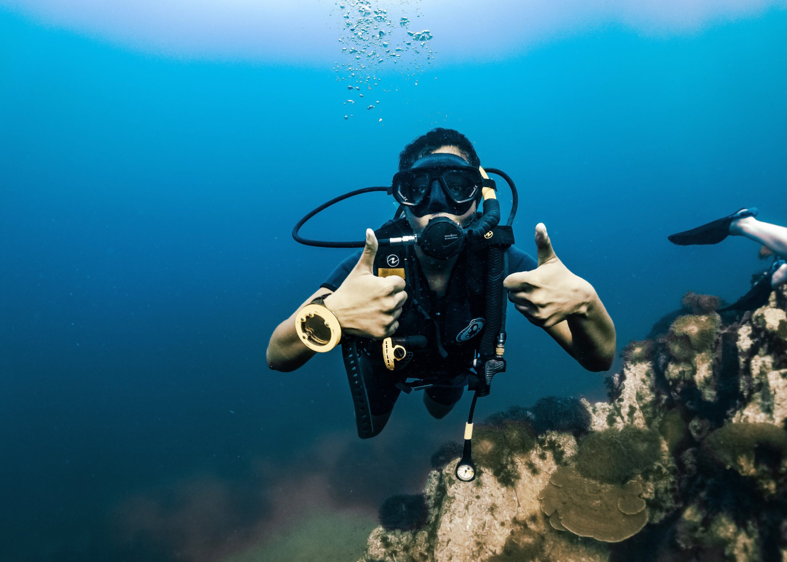 A scuba diver underwater giving a thumbs-up above a coral reef